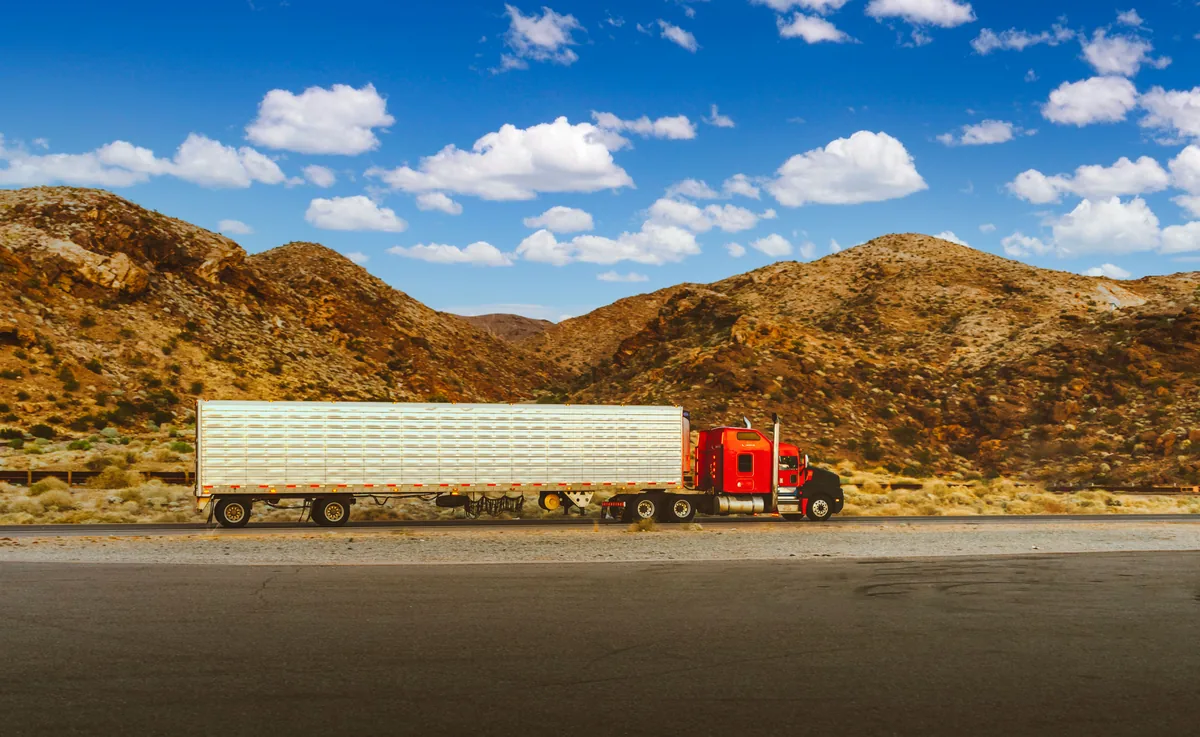 Red conventional semi-truck hauling a silver trailer through a desert landscape