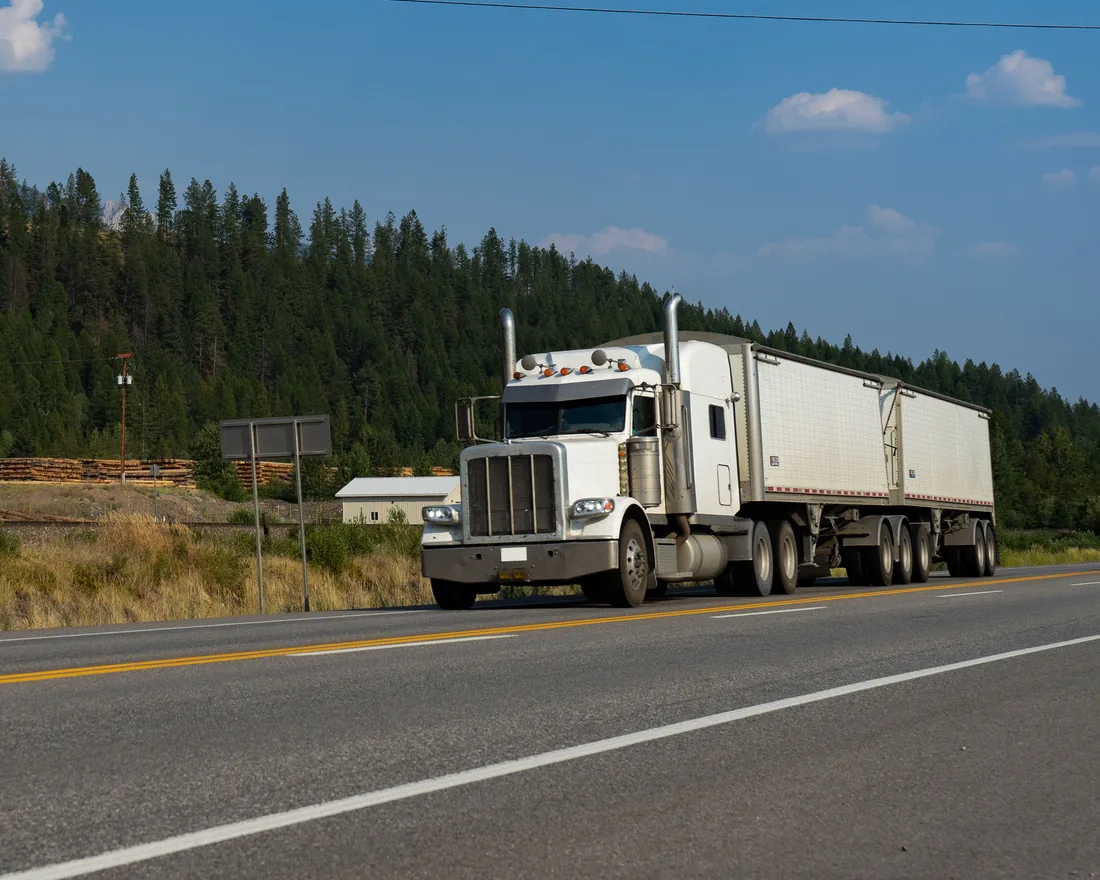 White conventional tractor-trailer on a forest-lined road in British Columbia